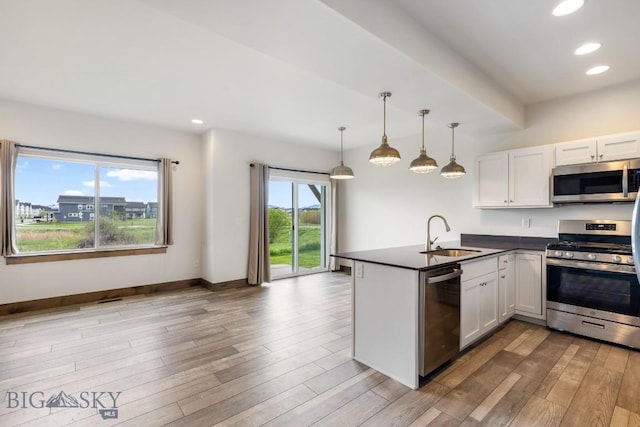 kitchen with a sink, appliances with stainless steel finishes, dark countertops, a peninsula, and white cabinetry