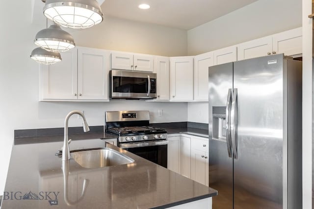 kitchen featuring stainless steel appliances, a sink, dark countertops, white cabinetry, and recessed lighting
