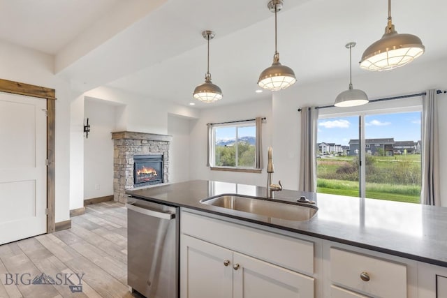kitchen featuring dishwasher, a sink, dark countertops, a stone fireplace, and recessed lighting