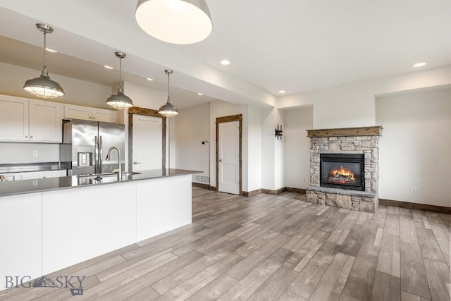 kitchen featuring stainless steel refrigerator with ice dispenser, a sink, recessed lighting, wood finished floors, and baseboards