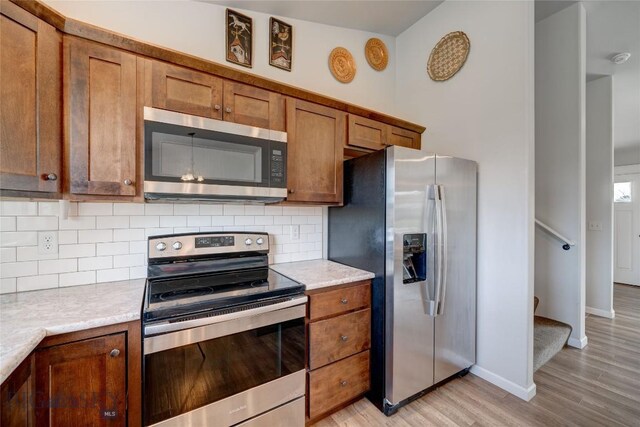 1510 Ingomar Blvd, Belgrade, MT 59714 - kitchen featuring appliances with stainless steel finishes, light wood-style flooring, brown cabinetry, decorative backsplash, and light countertops