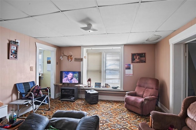 carpeted living room featuring a drop ceiling and baseboards