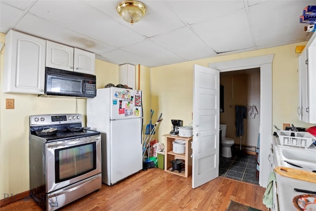 kitchen featuring black microwave, stainless steel electric range oven, freestanding refrigerator, a drop ceiling, and white cabinets