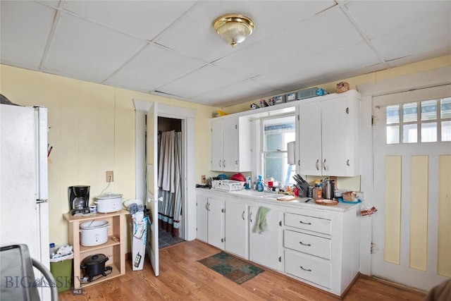 kitchen with freestanding refrigerator, light countertops, a paneled ceiling, white cabinetry, and light wood-style floors