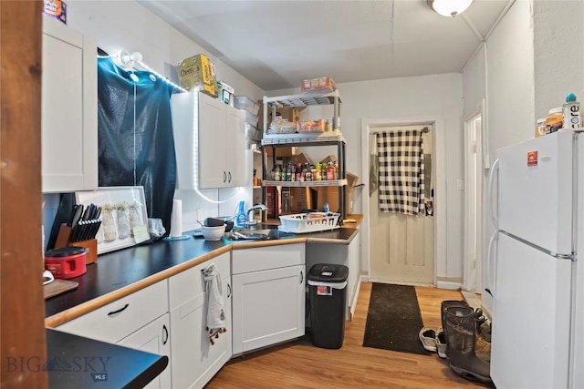 kitchen with freestanding refrigerator, a sink, light wood-style floors, and white cabinetry