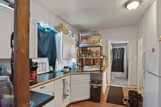 kitchen with freestanding refrigerator, light wood-type flooring, white cabinets, dark countertops, and a sink