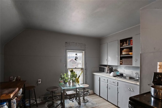 kitchen with a sink, stainless steel microwave, open shelves, light countertops, and light wood-style flooring