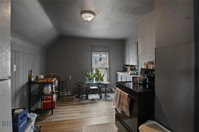 kitchen featuring black range with electric stovetop, light wood-style flooring, and vaulted ceiling