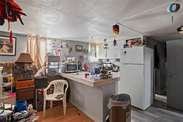 kitchen featuring freestanding refrigerator, stainless steel microwave, wood finished floors, a textured ceiling, and a peninsula