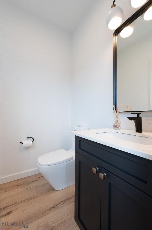 half bathroom with wood finished floors, vanity, toilet, and baseboards