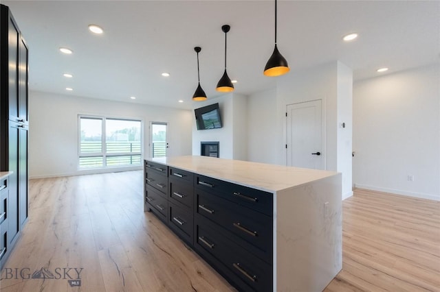 kitchen featuring light wood-style flooring, a fireplace, hanging light fixtures, baseboards, and recessed lighting