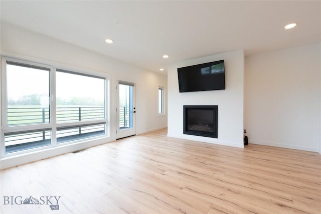 unfurnished living room featuring light wood finished floors, a glass covered fireplace, baseboards, and recessed lighting