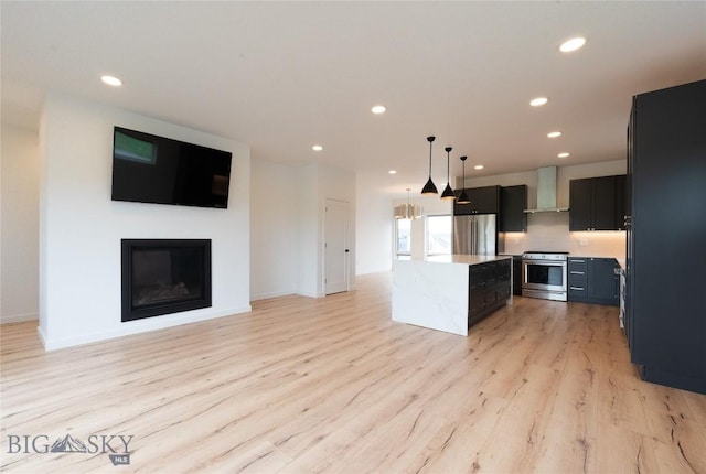 kitchen featuring wall chimney range hood, stainless steel appliances, a kitchen island, light wood-style floors, and recessed lighting