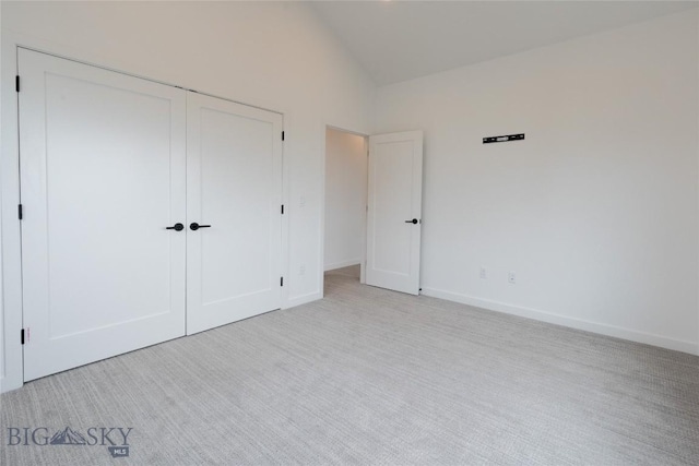 unfurnished bedroom featuring a closet, light colored carpet, vaulted ceiling, and baseboards