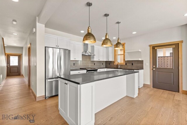 3164 S 15th Ave, Bozeman, MT 59715 - kitchen featuring appliances with stainless steel finishes, wall chimney exhaust hood, dark countertops, a kitchen island, and light wood-type flooring