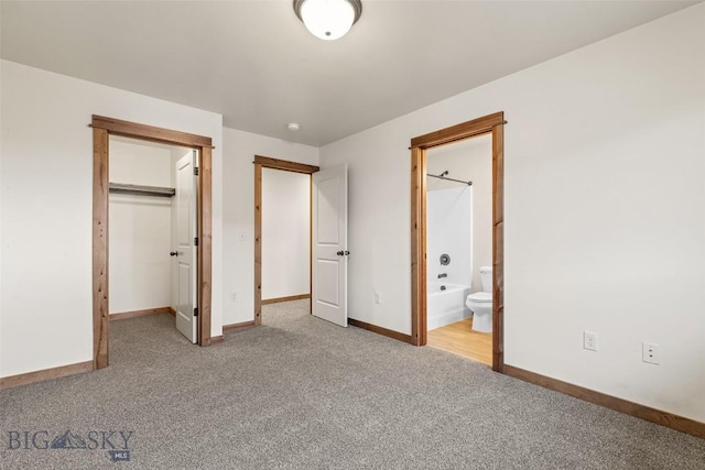 unfurnished bedroom with carpet, baseboards, a spacious closet, ensuite bathroom, and a closet