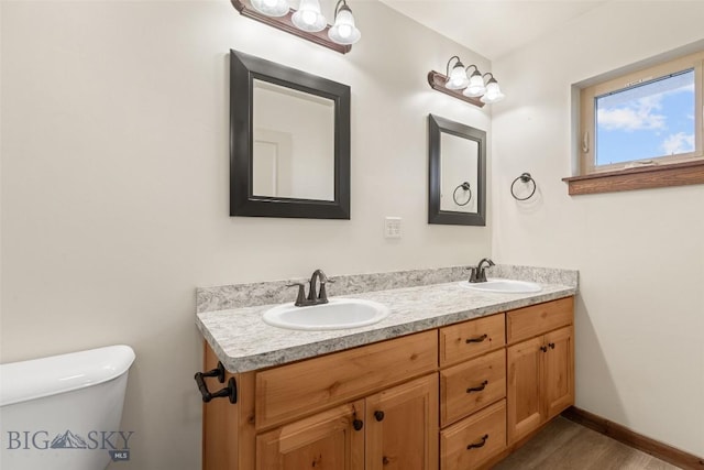 bathroom featuring toilet, double vanity, wood finished floors, and baseboards