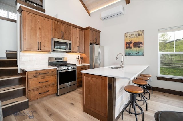 17450 Wilson Creek Rd, Gallatin Gateway, MT 59730 - kitchen featuring stainless steel appliances, a wall mounted air conditioner, brown cabinetry, a breakfast bar, and light wood-type flooring