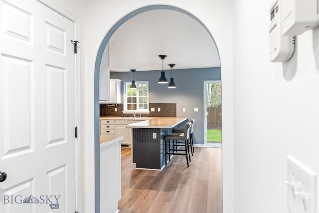 185 Chestnut Grove Ave, Bozeman, MT 59718 - kitchen featuring arched walkways, a kitchen breakfast bar, white cabinets, light wood-type flooring, and backsplash