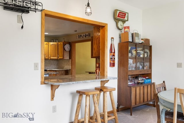 486 Jardine Rd, Jardine, MT 59030 - kitchen featuring brown cabinetry, backsplash, a breakfast bar, light colored carpet, and hanging light fixtures