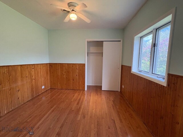 330 N Walnut St, Dillon, MT 59725 - unfurnished bedroom with a wainscoted wall, wood walls, wood finished floors, a closet, and a ceiling fan
