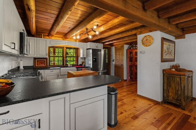 25 Big Chief Trl, Bozeman, MT 59718 - kitchen with stainless steel appliances, light wood finished floors, a peninsula, a wood ceiling with exposed beams, and dark countertops