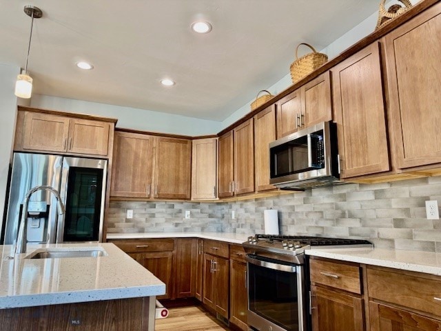920 Butler Creek Ave, Belgrade, MT 59714 - kitchen featuring stainless steel appliances, light stone counters, brown cabinetry, pendant lighting, and backsplash
