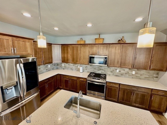 920 Butler Creek Ave, Belgrade, MT 59714 - kitchen featuring appliances with stainless steel finishes, a sink, pendant lighting, decorative backsplash, and light stone countertops