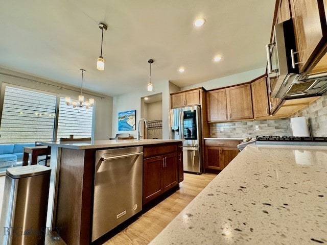 920 Butler Creek Ave, Belgrade, MT 59714 - kitchen featuring appliances with stainless steel finishes, a center island with sink, decorative backsplash, a chandelier, and light wood finished floors