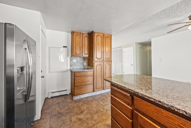34 Mammoth, Butte, MT 59701 - kitchen with stainless steel fridge, a baseboard heating unit, ceiling fan, brown cabinetry, and a textured ceiling