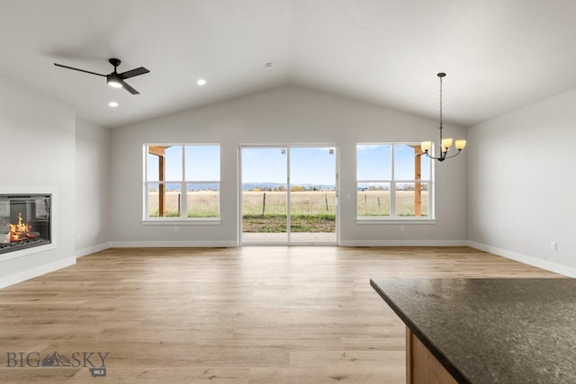 608 Spaniel Ln, Belgrade, MT 59714 - unfurnished living room with plenty of natural light, vaulted ceiling, a glass covered fireplace, a chandelier, and light wood finished floors