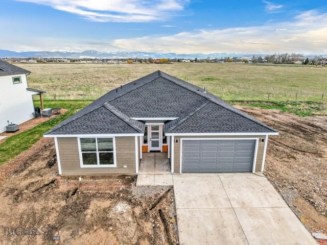 608 Spaniel Ln, Belgrade, MT 59714 - ranch-style home with a shingled roof, concrete driveway, an attached garage, central AC unit, and a rural view