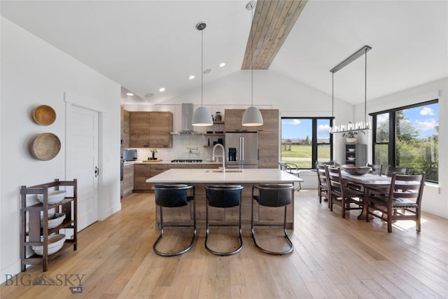 646 Arrow Trl, Bozeman, MT 59718 - kitchen featuring stainless steel refrigerator with ice dispenser, light countertops, light wood-type flooring, wall chimney exhaust hood, and a sink