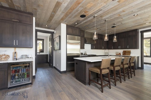 kitchen featuring stainless steel built in fridge, beverage cooler, wood ceiling, a breakfast bar area, and light countertops
