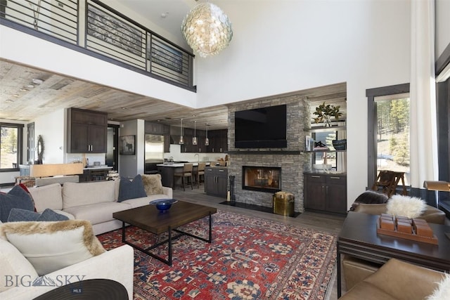 living area with a towering ceiling, wood finished floors, a fireplace, and a chandelier