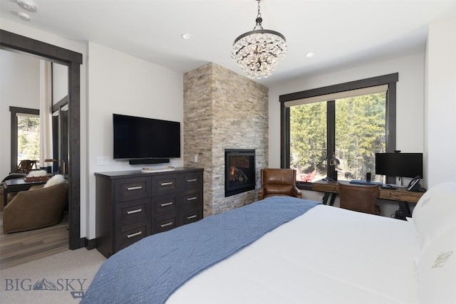 bedroom with a stone fireplace, a chandelier, recessed lighting, carpet flooring, and wood finished floors