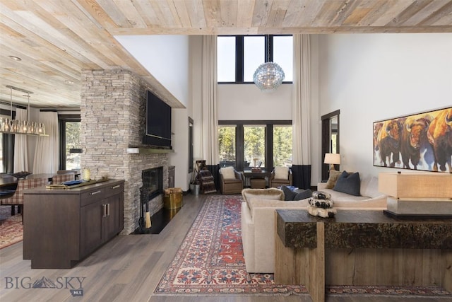 living area with wooden ceiling, a stone fireplace, wood finished floors, a chandelier, and a towering ceiling