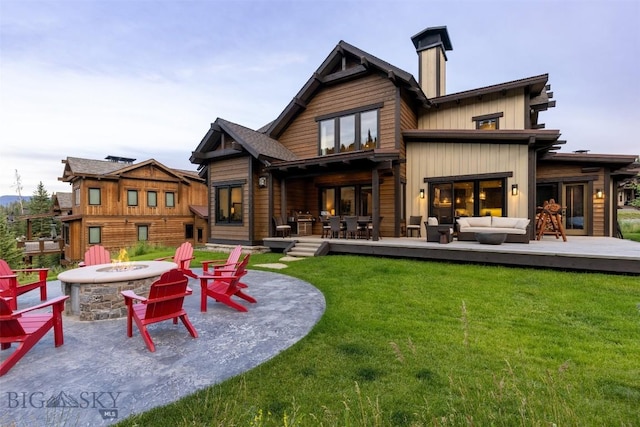 rear view of property featuring an outdoor living space with a fire pit, a yard, a chimney, and a deck