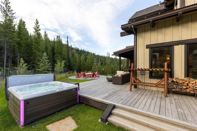 wooden terrace with a hot tub, a forest view, an outdoor living space, and a yard