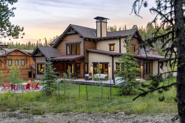 back of house featuring a fire pit, roof with shingles, a chimney, a lawn, and a patio area