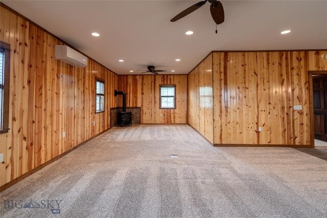 115AND117 Otter Creek Rd, Big Timber, MT 59011 - unfurnished living room with a wall mounted air conditioner, a ceiling fan, a wood stove, carpet floors, and wooden walls
