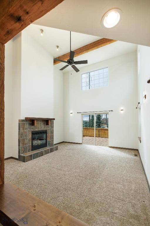 20 Prairie Grass B, Bozeman, MT 59718 - unfurnished living room featuring a tiled fireplace, a ceiling fan, carpet flooring, and a towering ceiling