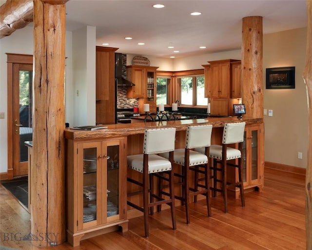 250 Petes Way, Big Sky, MT 59730 - kitchen with light wood-type flooring, a peninsula, brown cabinets, wall chimney range hood, and recessed lighting