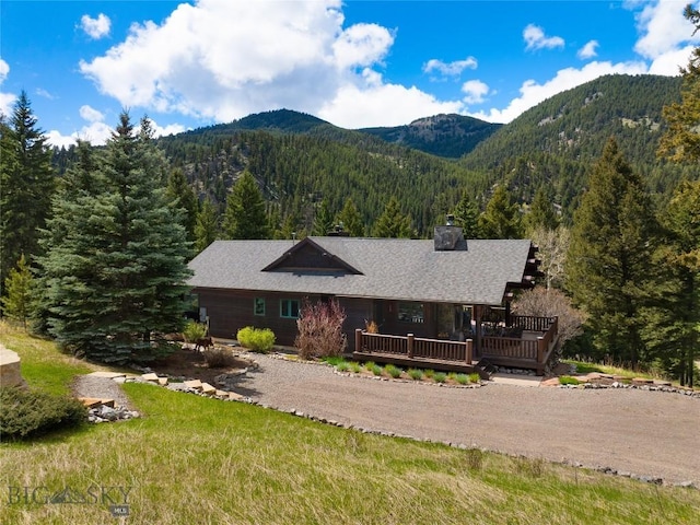 250 Petes Way, Big Sky, MT 59730 - view of front of home featuring a view of trees, a chimney, a deck with mountain view, and dirt driveway