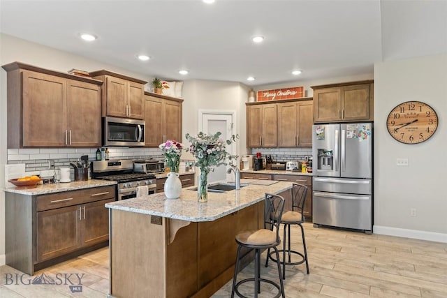 1711 Shelby Ave, Belgrade, MT 59714 - kitchen featuring stainless steel appliances, a sink, decorative backsplash, light stone countertops, and light wood finished floors
