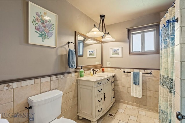 707 Montana St, Belgrade, MT 59714 - bathroom featuring tile walls, toilet, vanity, wainscoting, and stone finish floors