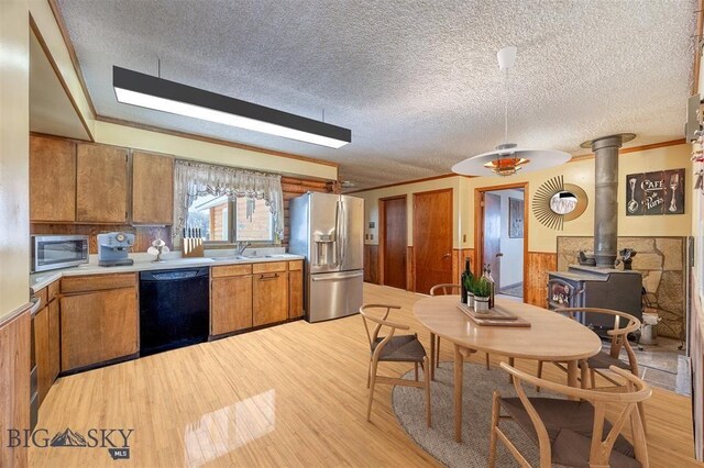 77 First Rd, Whitehall, MT 59759 - kitchen featuring appliances with stainless steel finishes, a wood stove, light wood-style flooring, brown cabinets, and a wainscoted wall