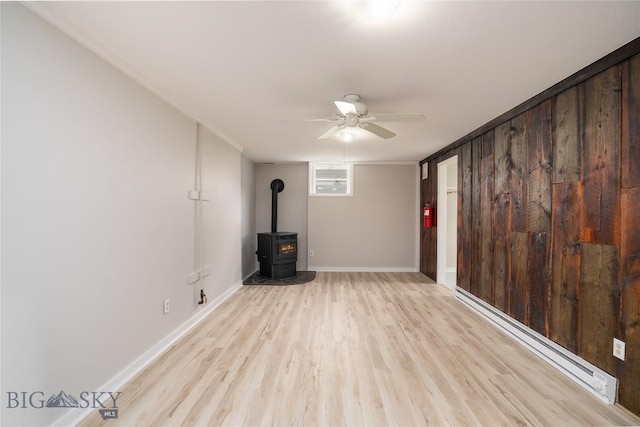 413 S Oak St, Townsend, MT 59752 - unfurnished living room featuring a ceiling fan, a wood stove, light wood finished floors, a baseboard radiator, and baseboards