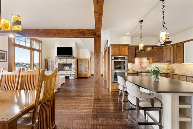 171 Brave Heart Loop, Bozeman, MT 59718 - kitchen with stainless steel double oven, a stone fireplace, dark countertops, decorative backsplash, and brown cabinetry