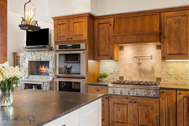 171 Brave Heart Loop, Bozeman, MT 59718 - kitchen with stainless steel appliances, a stone fireplace, dark countertops, and brown cabinets
